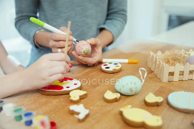 Fermer mère et fille décorant oeufs de Pâques et biscuits — Photo de stock
