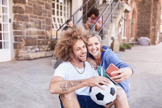 Пара з футбольним м'ячем бере селфі з телефоном — стокове фото