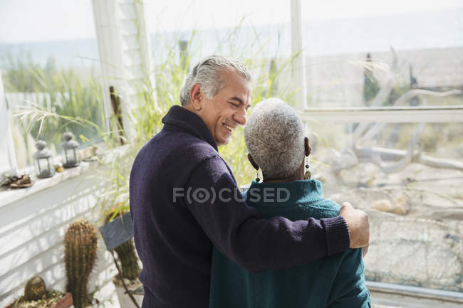 Старшая пара обнимается на солнечном крыльце пляжного домика — стоковое фото