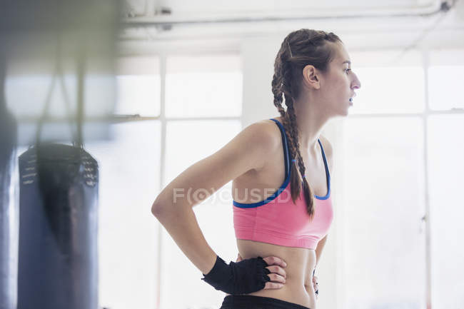 Уставшая молодая женщина тренируется, отдыхает руками на бедрах в тренажерном зале — стоковое фото