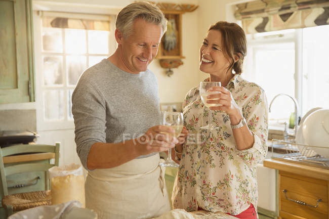 Улыбающаяся зрелая пара пьет вино и готовит на кухне — стоковое фото