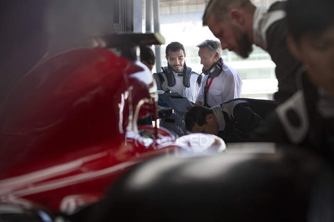 Gerente e fórmula um piloto de carro de corrida falando na garagem de reparação — Fotografia de Stock
