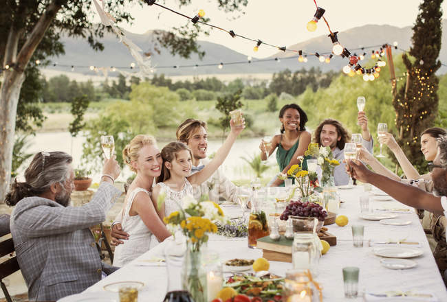 Pareja joven e invitados brindando con champán durante la recepción de la boda en el jardín doméstico - foto de stock