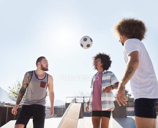 Чоловіки друзі грають у футбол на сонячному скейт-парку — стокове фото