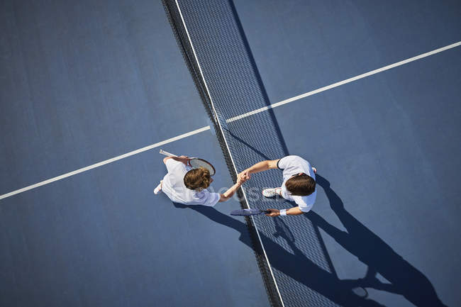 Перегляд зверху молодих тенісистів-чоловіків рукостискання в мережі на сонячно-блакитному тенісному корті — стокове фото