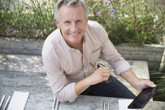 Портрет усміхненого старшого чоловіка, що використовує цифровий планшет на патіо — стокове фото