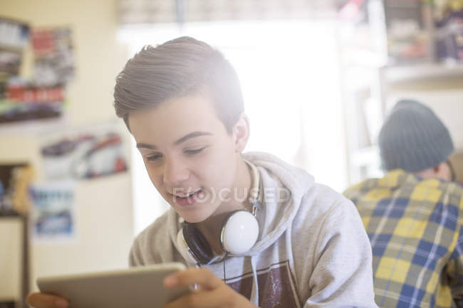 Dos chicos adolescentes sentados en la habitación y usando dispositivos electrónicos - foto de stock