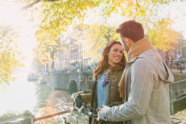 Smiling young couple with bicycle on bridge over sunny autumn canal in Amsterdam — Stock Photo