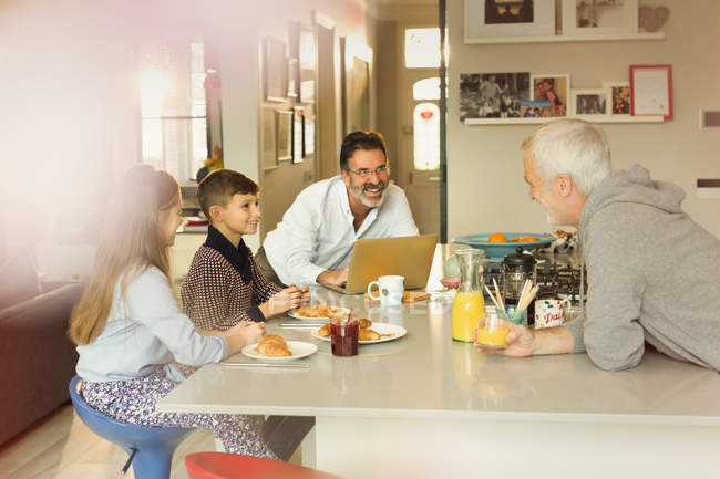 Hombres padres gay y niños disfrutando del desayuno en el mostrador de la cocina - foto de stock
