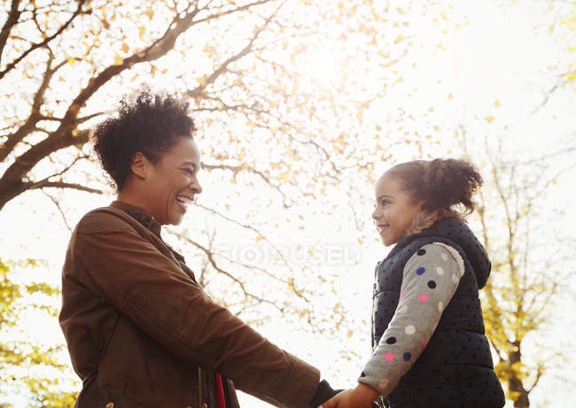 Affectionate mother and daughter holding hands in autumn park — Stock Photo