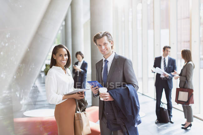 Retrato sonriente hombre de negocios y mujer de negocios en el vestíbulo de la oficina soleado - foto de stock
