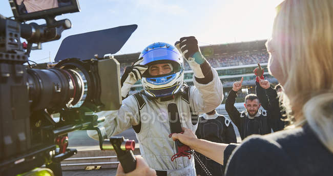 News reporter and cameraman interviewing formula one driver cheering, celebrating victory — Stock Photo