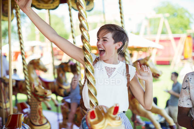 Mulher alegre sentada no cavalo no carrossel no parque de diversões — Fotografia de Stock