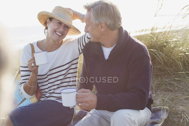Couple d'âge mûr boire du café dans l'herbe de plage ensoleillée — Photo de stock