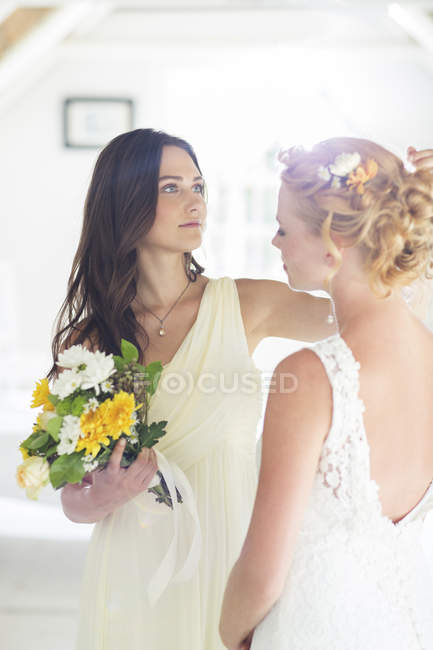 Bridesmaid helping bride with hairstyle in bedroom — Stock Photo