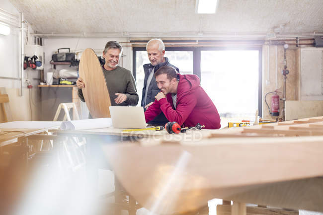 Carpinteiros masculinos usando laptop perto de barco de madeira na oficina — Fotografia de Stock