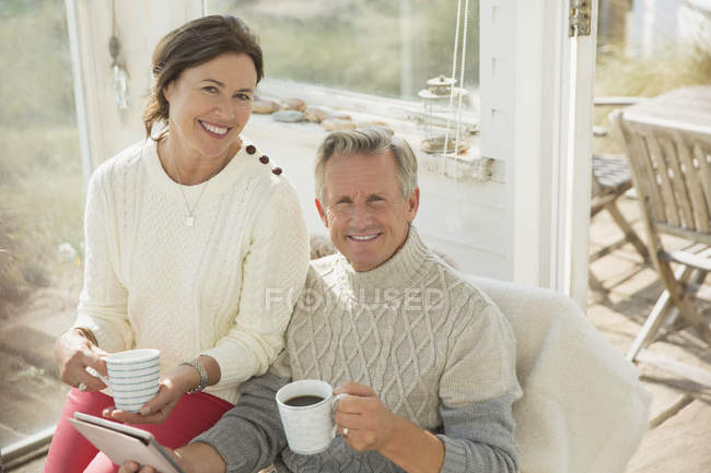 Portrait sourire couple d'âge mûr à l'aide d'une tablette numérique et boire du café sur le porche du soleil — Photo de stock