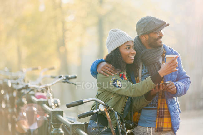 Young couple with bicycle drinking coffee and looking away along autumn railing, Amsterdam — Stock Photo