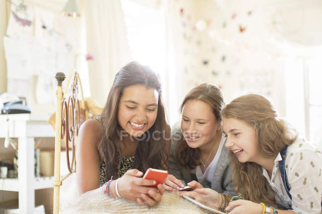 Three teenage girls using smartphone together while lying on bed in bedroom — Stock Photo