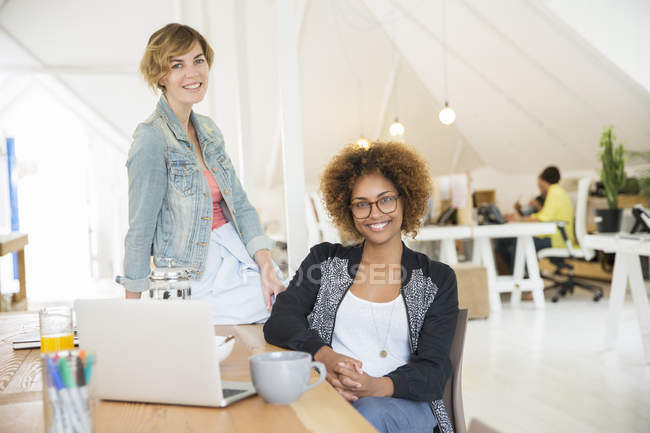 Portrait of women smiling in office with laptop on desk — Stock Photo