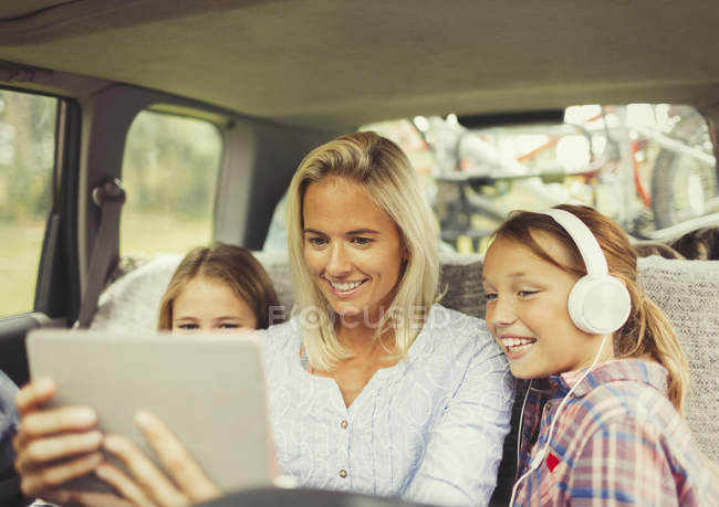 Mother and daughters watching video on digital tablet in back seat of car — Stock Photo