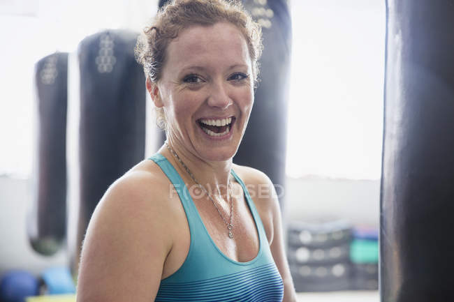 Portrait laughing female boxer standing at punching bag in gym — Stock Photo