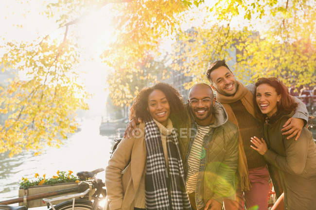 Ritratto amici sorridenti che si abbracciano al soleggiato canale autunnale — Foto stock