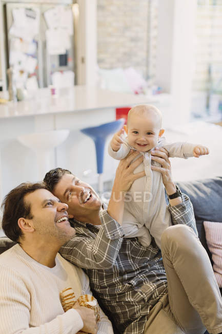 Retrato juguetón lindo bebé hijo con macho gay padres - foto de stock