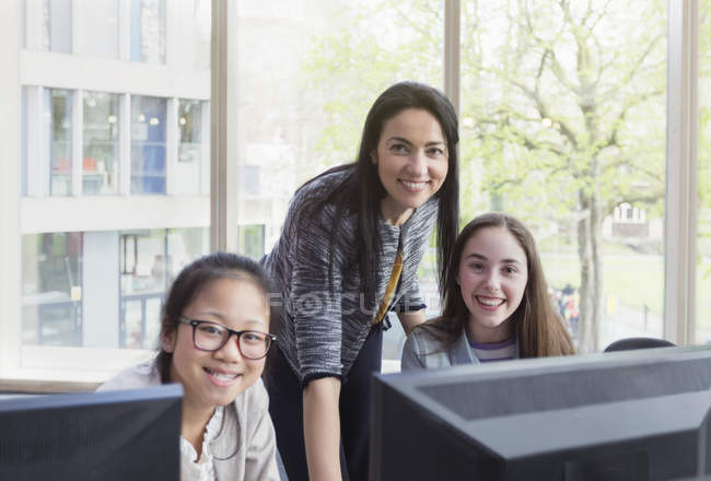 Portrait confident, smiling female teacher and girl students researching at computer in library — Stock Photo