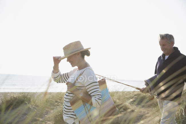 Casal maduro com vara de pesca andando em ensolarado verão praia grama — Fotografia de Stock