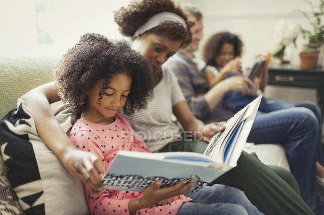 Родители читают книги с дочерьми на диване в гостиной — стоковое фото