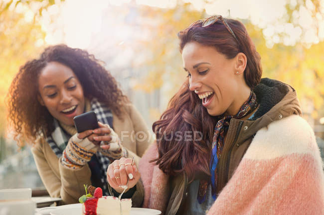 Giovane donna con fotocamera telefono fotografare amico mangiare cheesecake dessert al caffè marciapiede — Foto stock