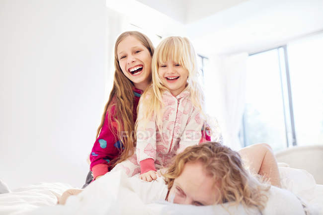 Lachende Schwestern auf Vater im Bett — Stockfoto