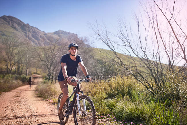 Jovem mountain bike em ensolarado, estrada de terra remota — Fotografia de Stock