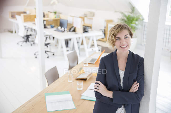 Retrato de la mujer apoyada en la columna en la oficina y sonriendo - foto de stock