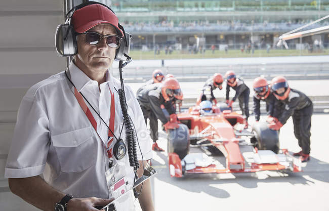 Retrato gerente serio con la fórmula de un coche de carreras y la tripulación de boxes en segundo plano - foto de stock