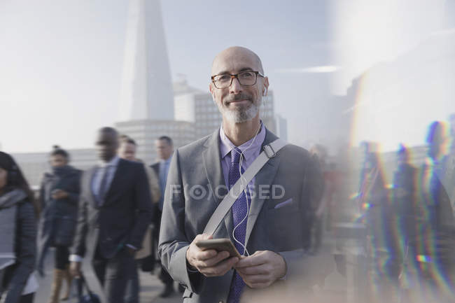 Portrait confident businessman listening to music with cell phone and headphones on busy urban street — Stock Photo