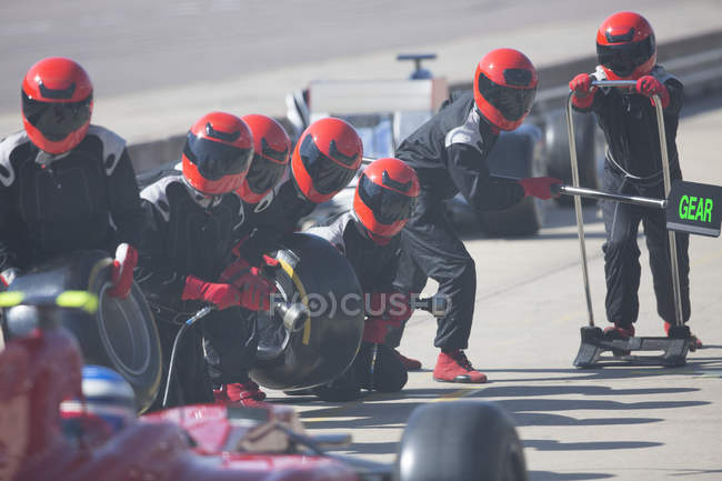 Tripulación de hoyos con neumáticos listos para acercarse a la fórmula de un coche de carreras en pit lane - foto de stock
