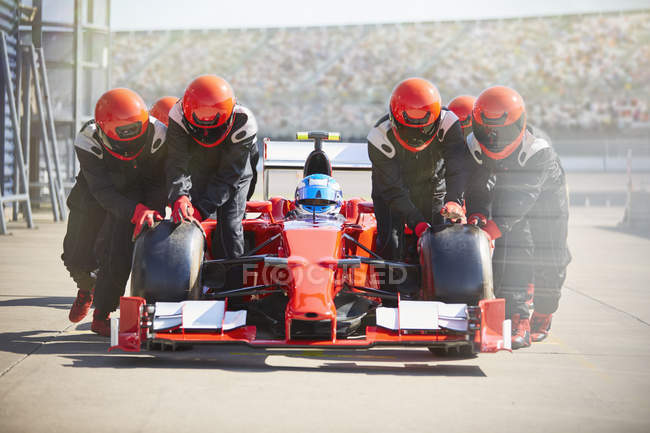 Pit crew empujando fórmula un coche de carreras fuera de pit lane - foto de stock