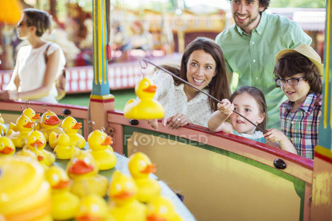 Los padres con dos hijos se divierten con el juego de pesca en el parque de atracciones - foto de stock