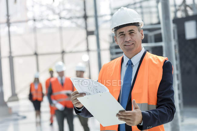 Porträt lächelnder Geschäftsmann mit Klemmbrett auf Baustelle — Stockfoto