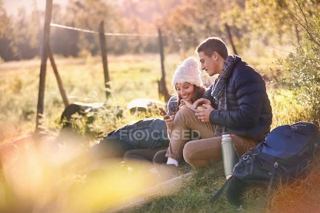 Young couple hikers resting in sunny grass using cell phone and digital tablet — Stock Photo