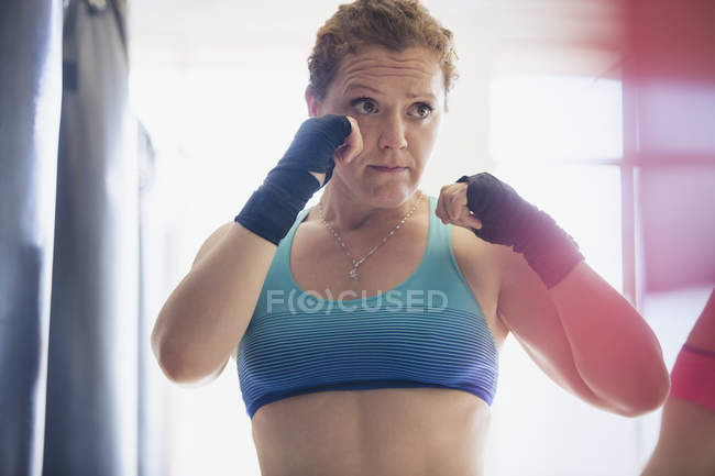 Boxeadora femenina decidida con muñequeras en postura de lucha en el gimnasio - foto de stock