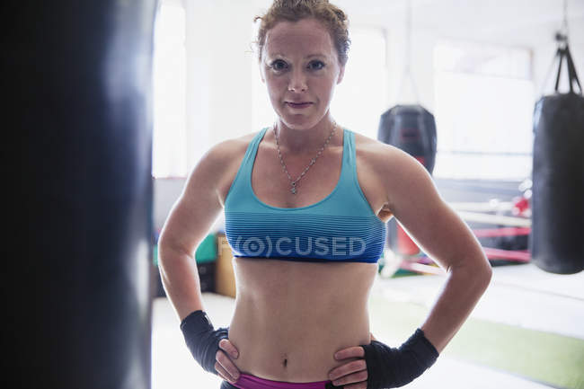 Retrato confiante, difícil boxeador feminino em pé no saco de perfuração no ginásio — Fotografia de Stock