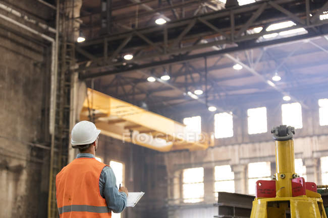 Stahlarbeiter mit Klemmbrett schaut in Fabrik nach oben — Stockfoto
