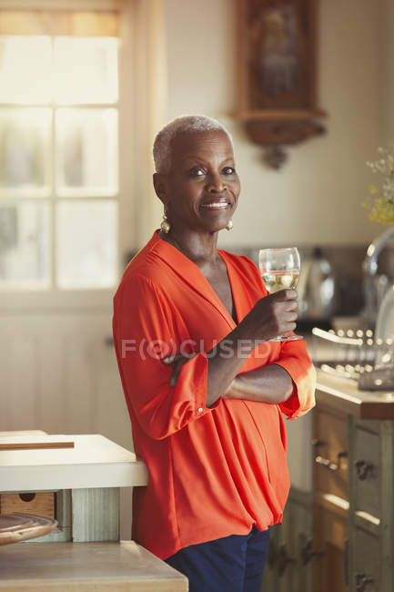 Портрет усміхненої старшої жінки, що п'є вино на кухні — стокове фото