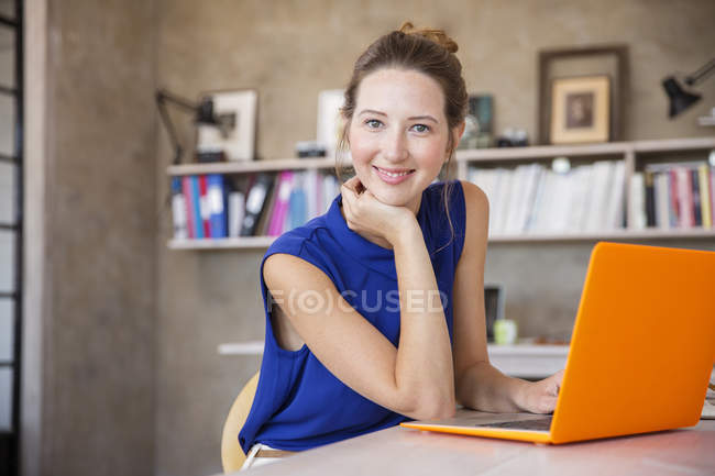 Портрет молодой женщины с оранжевым ноутбуком сидит в домашнем офисе — стоковое фото