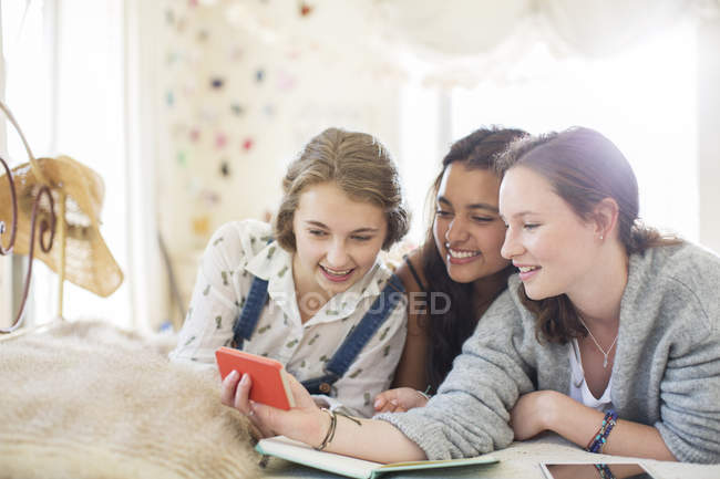 Three teenage girls using smartphone together while lying on bed — Stock Photo