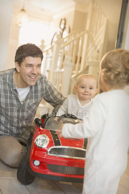 Padre e hijos bebés jugando con coche de juguete - foto de stock