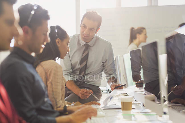 Male supervisor talking to female telemarketer wearing headset at computer in office — Stock Photo